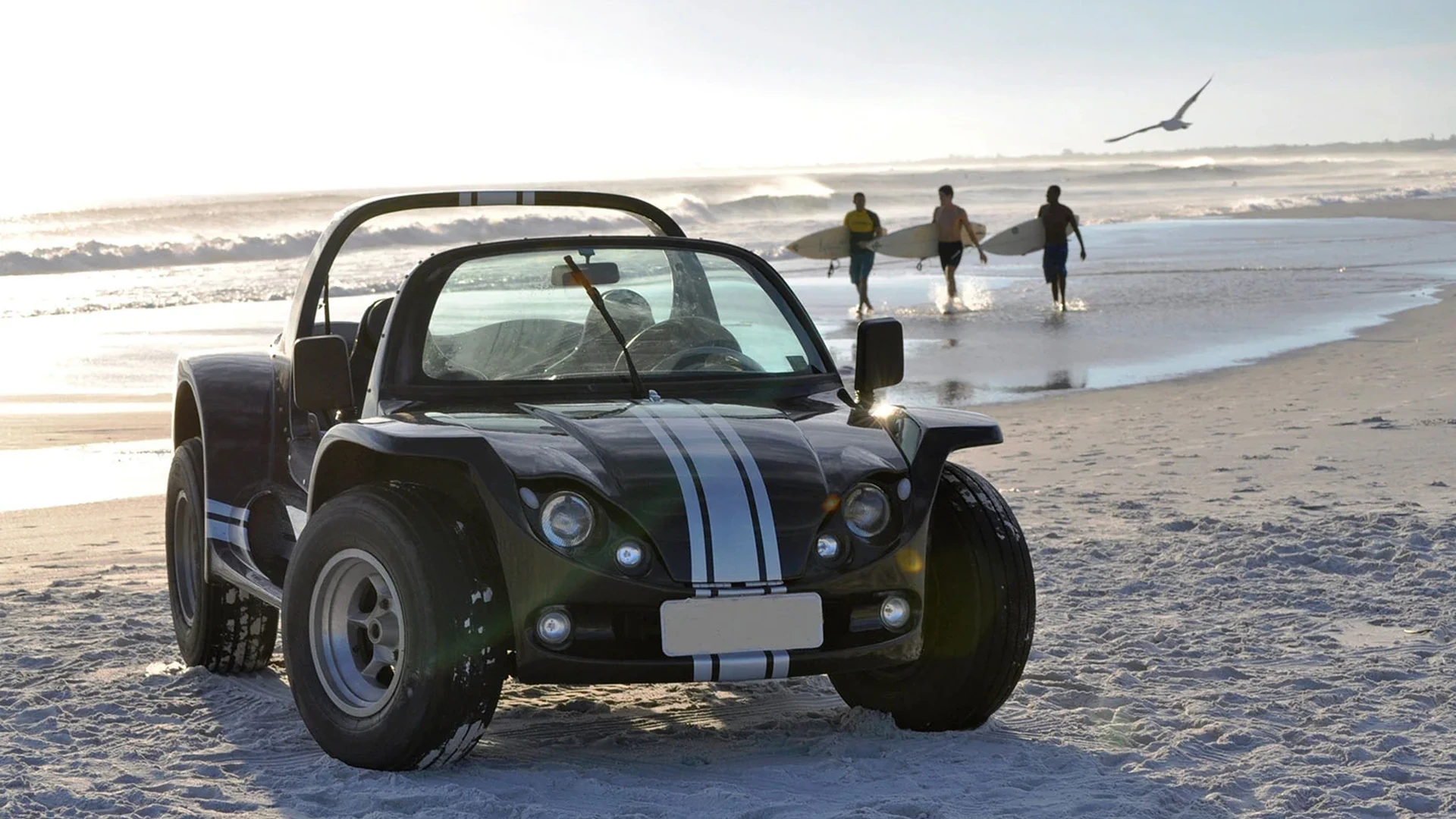 Buggy preto estacionado na areia da praia em Búzios, com surfistas caminhando e o mar ao fundo
